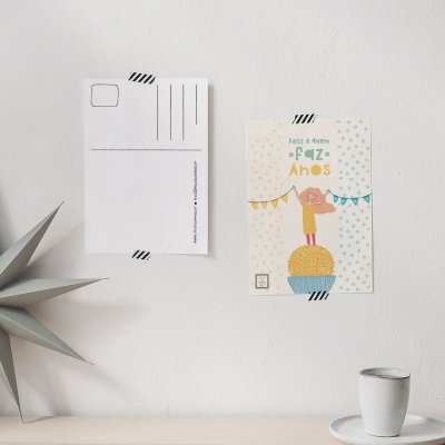 Postais decorativos numa parede branca, com uma estrela de papel cinza e um copo branco sobre pires numa superfície clara.