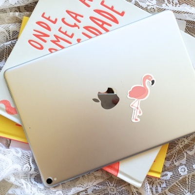 Tablet prateado com autocolante de flamingo em cima de livros sobre tecido rendado branco