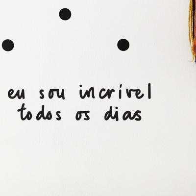 Parede branca com decalques pretos e texto motivacional em português.