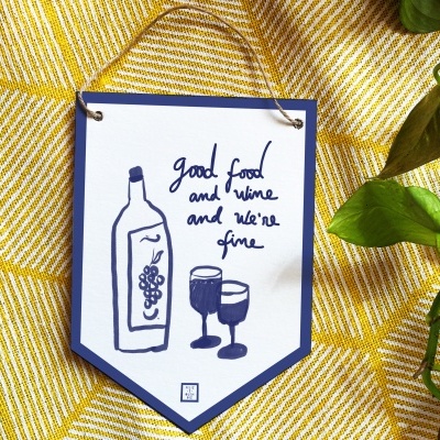 Pendão decorativo branco e azul com desenho de garrafa de vinho e taças, sobre tecido amarelo