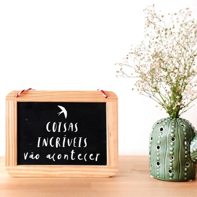 Lousa com frase inspiradora e vaso de cacto com flores secas sobre mesa de madeira