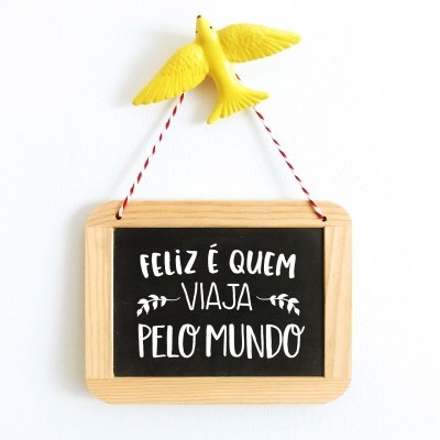 Placa decorativa de madeira com frase em português sobre viagem e pássaro amarelo