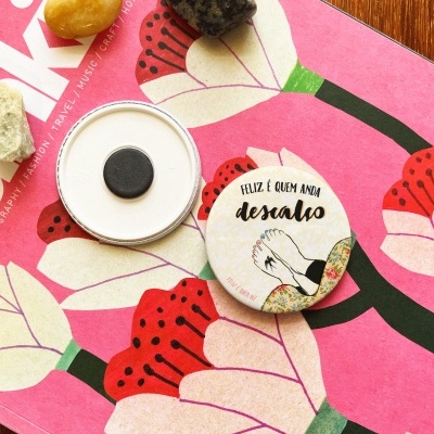 Dois botões redondos com texto e desenho em cima de revista rosa com flores e três pedras