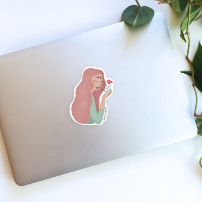 Portátil cinza com autocolante de mulher e planta verde ao lado.