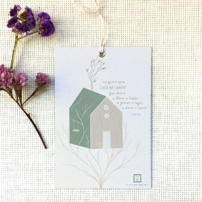 Etiqueta decorativa com desenho de casas e texto em francês sobre tecido cru com ramos secos lilás ao lado