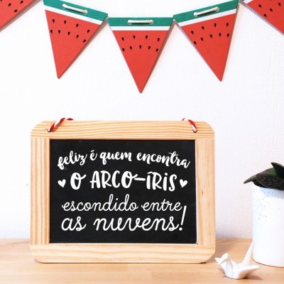 Placa decorativa com mensagem inspiradora em português, guirlanda vermelha com verde e vaso branco com planta.