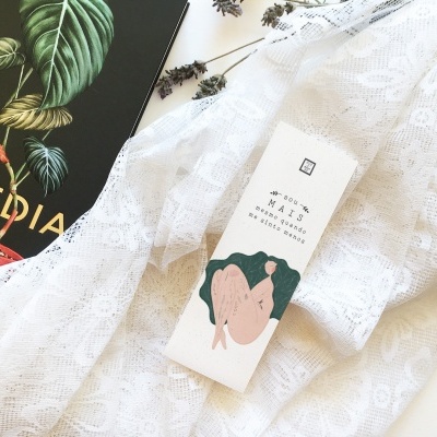 Caixa de bálsamo sólido sobre tecido rendado branco ao lado de livro preto com folhas verdes