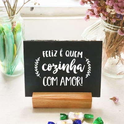 Cartaz preto com texto branco em suporte de madeira entre doces e frascos de flores secas