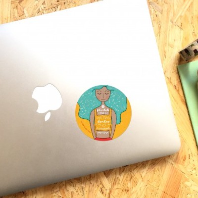 Computador portátil prateado com autocolante redondo colorido e acessórios sobre mesa de madeira