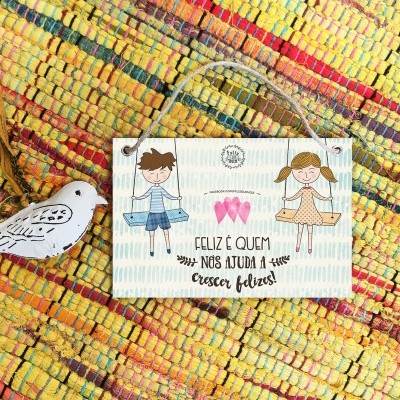 Placa decorativa em madeira com ilustração de crianças e texto, sobre tapete colorido, ao lado de figura de pássaro em madeira