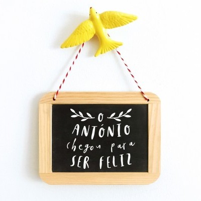 Placard pequeno de madeira com texto em português e pomba amarela suspensa