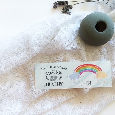 Etiqueta com texto e arco-íris sobre tecido florido branco e vaso cinza