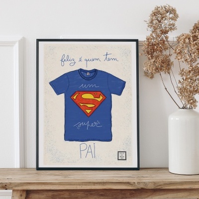 Moldura com ilustração de t-shirt azul com símbolo do Super-Homem e texto sobre a figura de uma mesa de madeira rústica com vaso branco