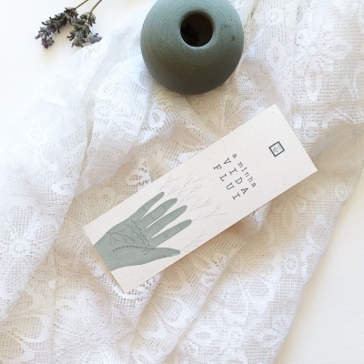 Saco branco com padrão floral, peça cerâmica verde redonda e cartão com desenho de mão e texto