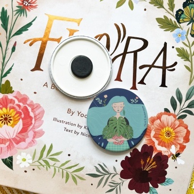 Capa do livro 'Flora' com flores ilustradas e dois bottons redondos disponíveis.