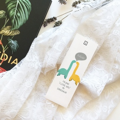 Caixa branca com desenhos de dinossauros em pano rendado ao lado de livro preto com folhas