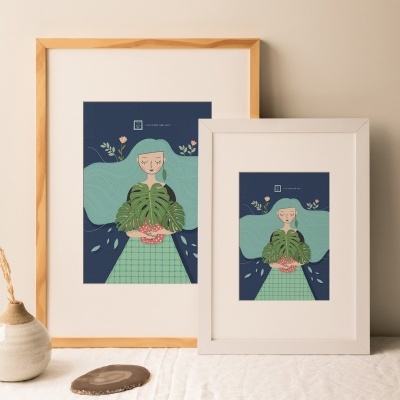 Dois quadros com ilustração de personagem segurando planta em molduras de madeira clara e branca sobre mesa com vaso e planta seca