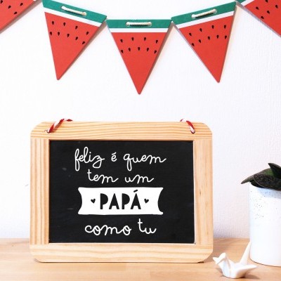 Quadro-negro emoldurado com mensagem para pai, planta em vaso branco e decoração de bandeirolas de melancia