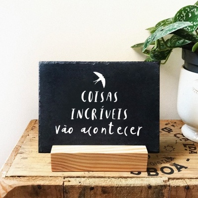 Placa decorativa preta com texto branco e vaso branco com planta verde