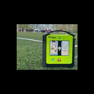 Desfibrilhador externo automático preto e verde com instruções visuais colocado em campo de relva artificial