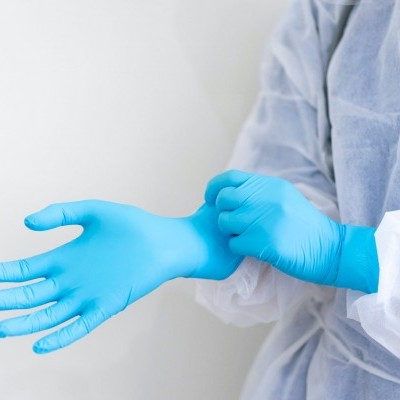 Pessoa a vestir luvas descartáveis azuis com bata protetora branca e azul