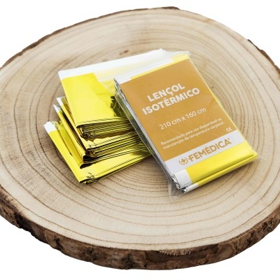 Conjunto de lençóis isotérmicos metálicos dourados com embalagem e etiqueta sobre base de madeira