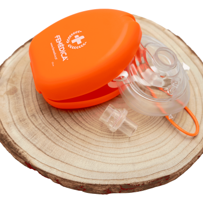 Máscara de reanimação transparente com estojo laranja FEMEDICA sobre suporte de madeira