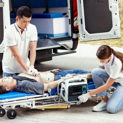 Pessoas a socorrer rapaz numa maca azul junto a ambulância.