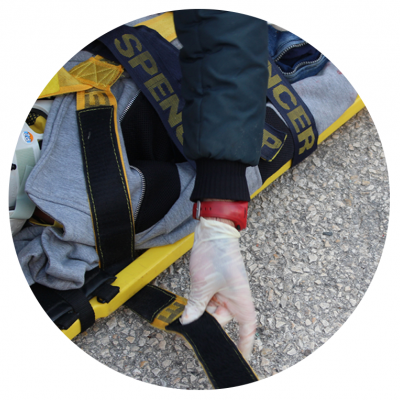 Pessoa com luva a ajustar cinta numa maca amarela e azul sobre chão de asfalto