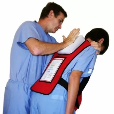 Dois homens com roupa médica azuis, um a aplicar manobra de Heimlich num manequim com colete de simulação vermelho e texto instrutivo nas costas.