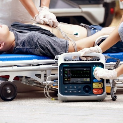 Desfibrilhador automático externo na ambulância com paciente deitada e profissional médico a operar.