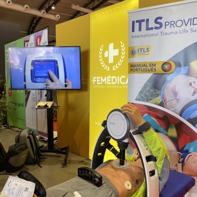 Manequim azul com dispositivo médico, cartaz FEMÉDICA amarelo e banner ITLS em feira