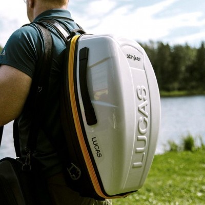 Mochila rígida branca com LUCAS em relevo, usada ao ar livre perto de um lago