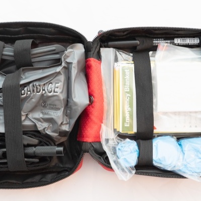 Estojo médico vermelho aberto com bandagens, tesoura e outros produtos.