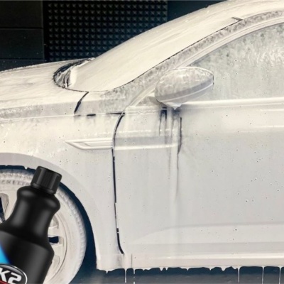 Carro branco coberto por espuma de lavagem com garrafa K2 em primeiro plano