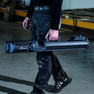 Pessoa com calças de trabalho e sapatos de segurança segurando ferramenta preta SCANGRIP em oficina