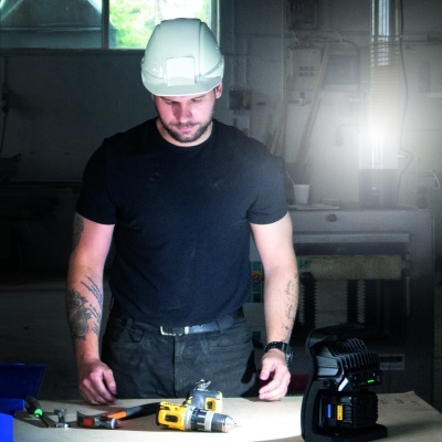 Homem com capacete de segurança branco e ferramentas numa bancada de oficina