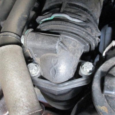 Componente automóvel em plástico preto com parafusos metálicos em motor sujo