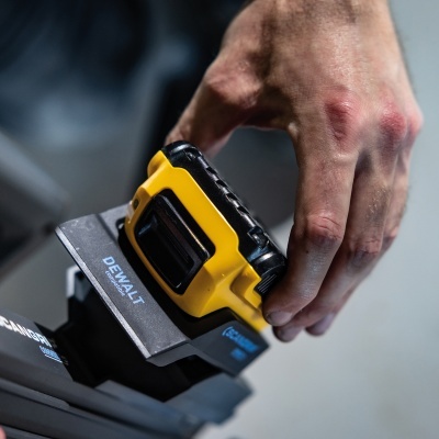 Bateria recarregável DEWALT amarela e preta numa base cinzenta com texto DEWALT Compatible e mão masculina a segurar