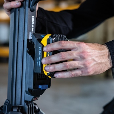 Mão segurando bateria amarela e preta SCANGRIP CONNECT em aparelho cinzento com botão azul PUSH