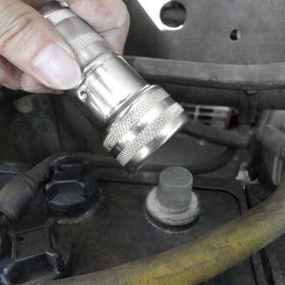 Mão segurando ferramenta metálica sobre bateria de carro