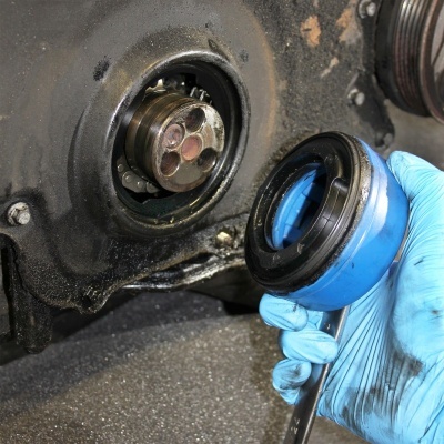 Peça metálica de mecanismo automóvel com mão enluvada a segurar tampa azul.