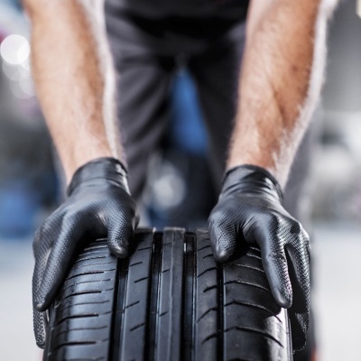 Pneus de carro pretos com padrão de banda de rodagem sendo segurados por mãos com luvas pretas