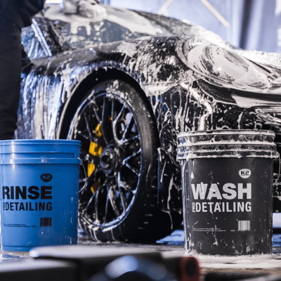Carro preto em lavagem com dois baldes, azul e preto, etiquetados RINSE pro DETAILING e WASH pro DETAILING.