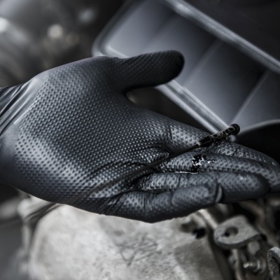 Mão com luva preta segurando vareta de óleo em motor de carro