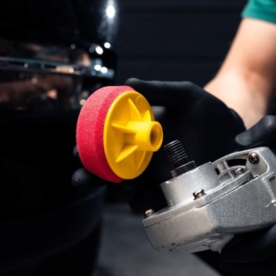 Espuma de polimento vermelha com suporte amarelo para polidor elétrico em mãos com luvas pretas