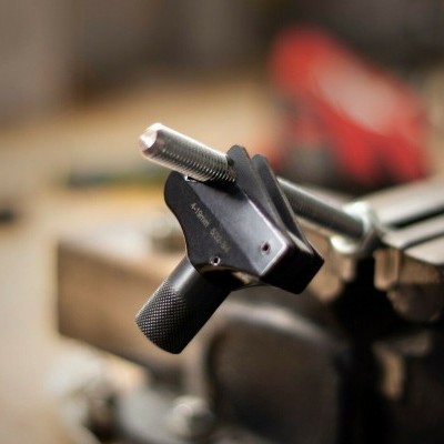 Peça metálica preta com parafuso prateado presa em morsa de metal em oficina