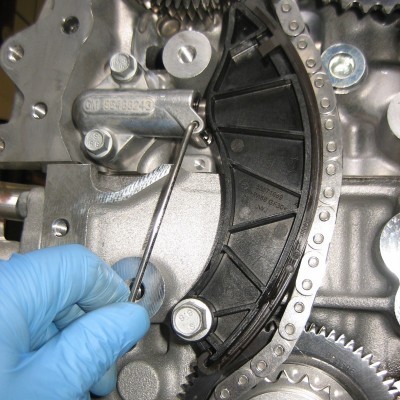 Peças metálicas de motor com corrente e mão com luva azul segurando ferramenta