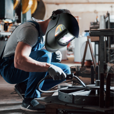 Homem a soldar metal numa oficina com máscara de soldadura preta