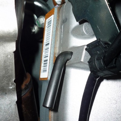 Peça metálica com tubo de borracha preto e etiqueta com código de barras